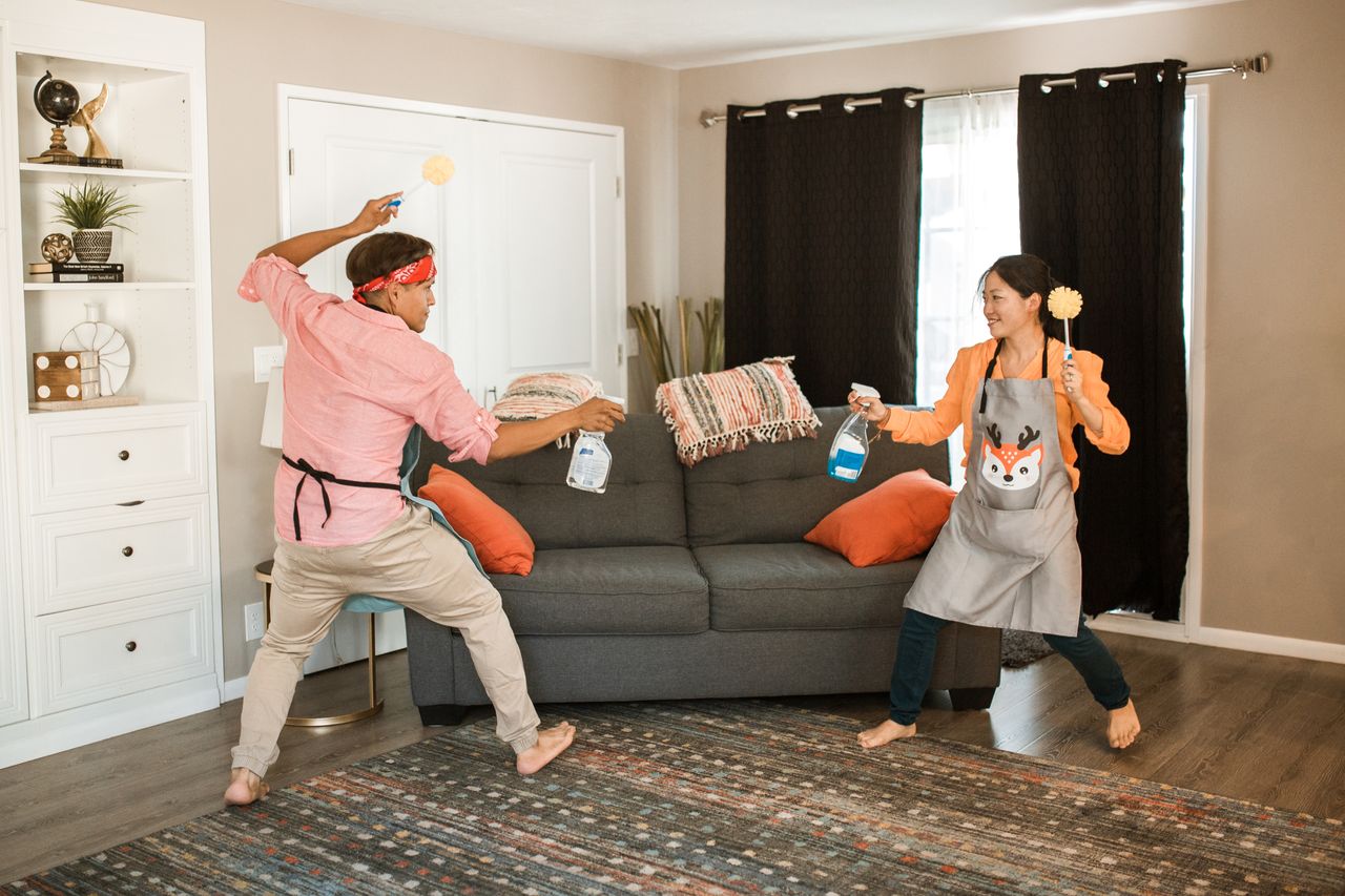 services-02 A joyful couple engages in a playful cleaning fight in their living room, showcasing light-hearted domestic life.
