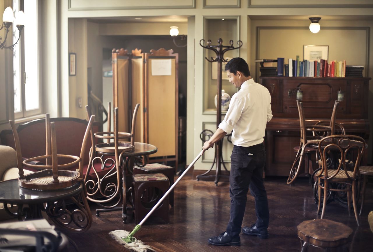 services-img Side view of young ethnic male in uniform cleaning floor with mop while working in retro styled restaurant